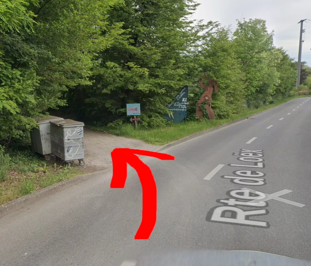 Une flèche rouge montre l’entrée du chemin forestier à gauche, juste devant la statue en fer de Mamajah.